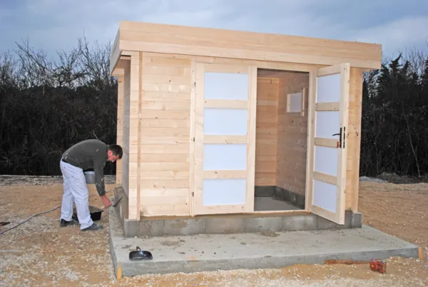 Abri en bois clair en cours de montage sur une dalle béton