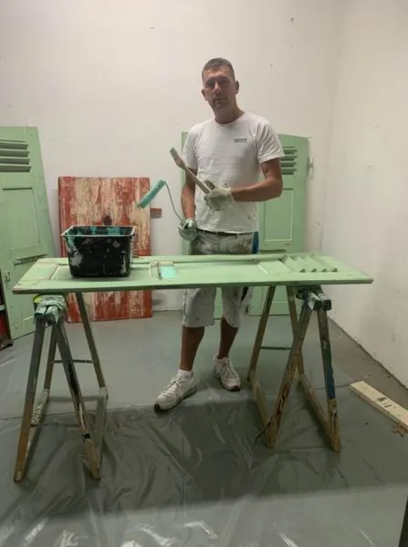 Dans l’atelier, un volet couché sur deux tréteaux, sol bâché