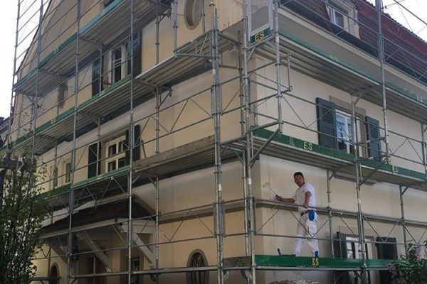 Échafaudage monté sur toute une maison ancienne, peintre au travail en hauteur