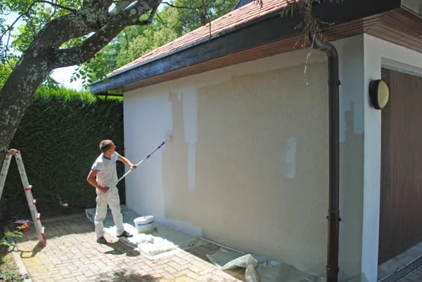 Mur d’une annexe traité au pulvérisateur, une haie à côté