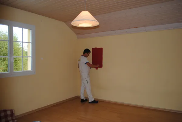 Un seul mur en rouge dans un séjour clair, parquet sous bâche