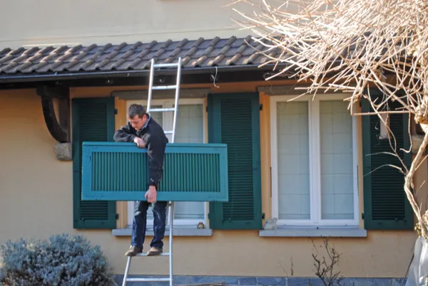 Volet bleu-vert repeint sur place, le peintre perché sur son échelle
